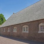 Oude bakstenen schuur met zadeldak en bomen