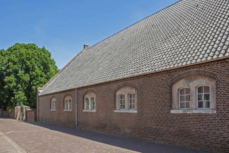 Oude bakstenen schuur met zadeldak en bomen
