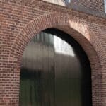 Oude bakstenen poort met groen geschilderde deur.